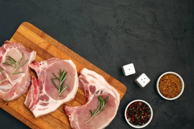 Kesme tahtasında çiğ domuz eti ve siyah arka planda baharatlar. Taze et. Üst görünüm