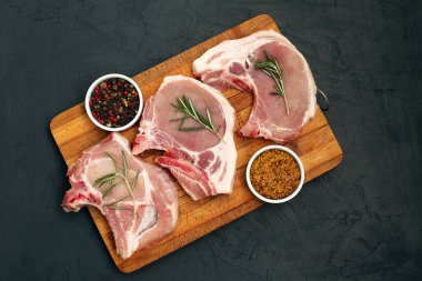 Kesme tahtasında çiğ domuz eti ve siyah arka planda baharatlar. Taze et. Üst görünüm