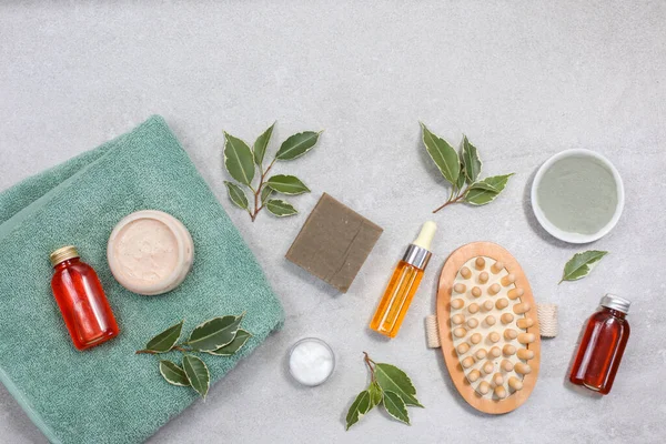Spa product composition with cosmetics, sea salt, towel and leaves at stone table. Body care and hygiene. Flat lay image with copy space.