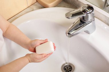 Çocuk ellerini sabunla yıkıyor musluğun altında suyla.