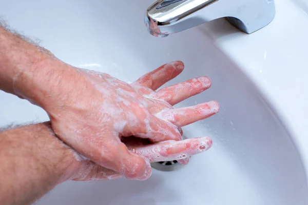 A Man is washing his hands with soap in bathroom. Man\'s hand close up. Hand disinfection and treatment for coronavirus. Quarantine rules. Personal hygiene
