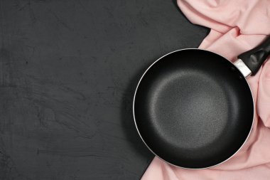 Siyah masasında pembe mutfak havlusu olan boş bir tava. Üst Manzara. Boşluğu kopyala.