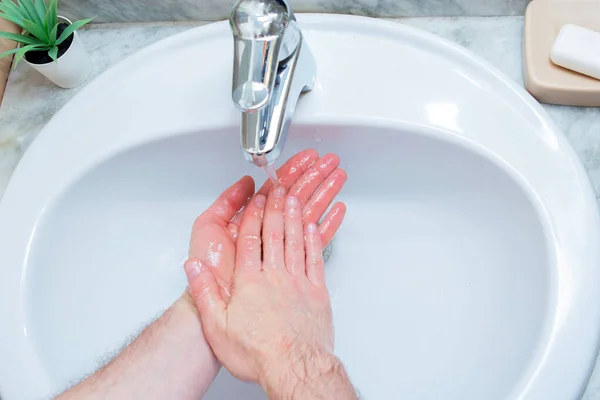 A Man is washing his hands with soap in bathroom. Man\'s hand close up. Hand disinfection and treatment for coronavirus. Quarantine rules. Personal hygiene