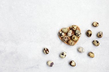 Küçük bıldırcın yumurtaları ahşap kasede, hafif taş arka planda kalp şeklinde. Eko ürünler. Boşluğu kopyala