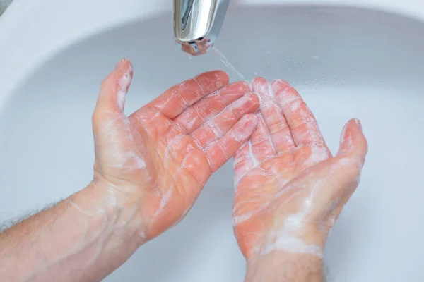 Adam banyo lavabosunun altında ellerini sabunla yıkıyor. Yakın plan el dezenfeksiyonu ve koronavirüs tedavisi. Karantina kuralları. Kişisel temizlik.