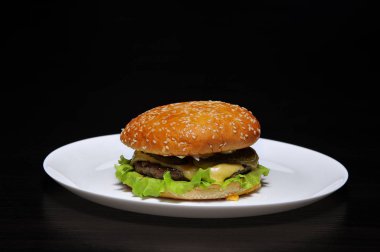 siyah arka plan üzerine beyaz bir tabak taze lezzetli burger