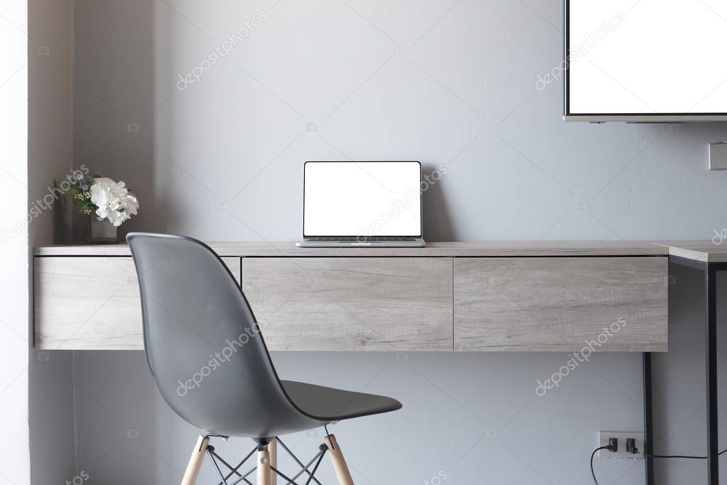 Laptop computer on wooden desk with empty chair and tv in white 