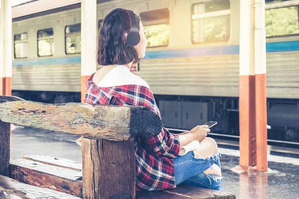 Young travel sitting at railway platform and listen music waitin