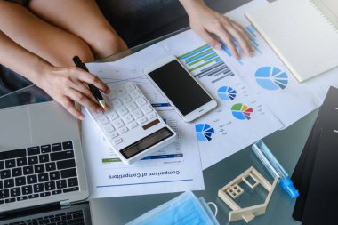 Ev konseptinden ahşap masa başı işlerde matematik finansmanı için hesap makinesi ve laptop kullanan iş kadını kapat