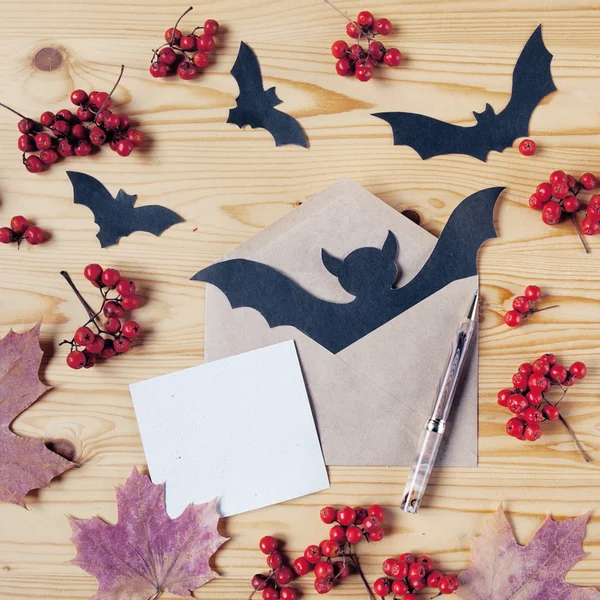 Draufsicht auf eine hölzerne halloween-Tischplatte mit Papier, Stift, Umschlag, Fledermäusen, Beeren und Ahornblättern. mit Kopierraum. — Stockfoto