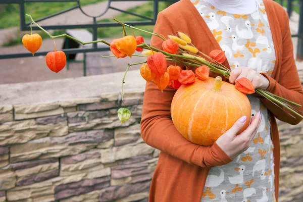 Genç kız bir turuncu kabak holding ve çiçekler.
