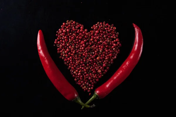 Два красных перца чили на черном фоне. Горошек в форме сердца — стоковое фото