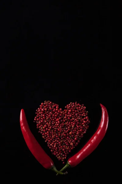 Два красных перца чили на черном фоне. Горошек в форме сердца — стоковое фото