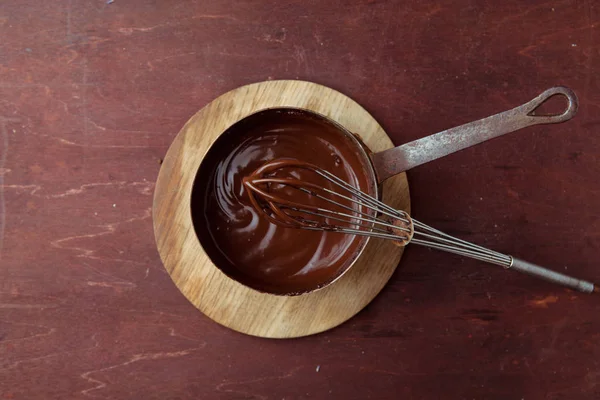 Ahşap arka plan üzerinde çırpma teli ile tavada eritilmiş çikolata girdap