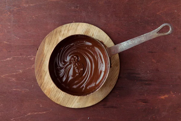 Растаявший шоколадный вихрь в кастрюле на деревянном фоне — стоковое фото