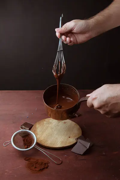 Мужские руки мешают расплавленный шоколадный вихрь в кастрюле на деревянном фоне — стоковое фото
