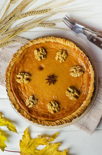 Pumpkin homemade vegan pie and spices cinnamon, anis, orange pumpkins with yelllow dry autumn leaves decor on dark table background.