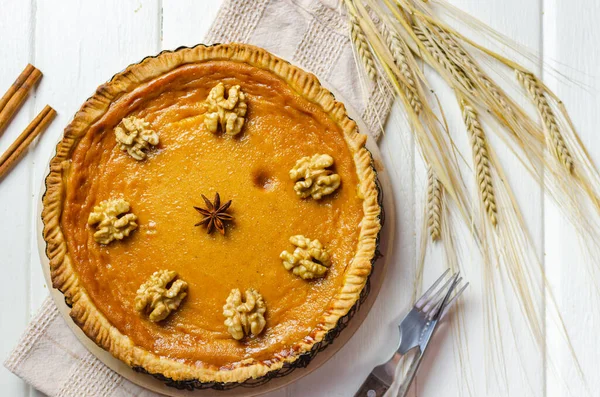 Pumpkin homemade vegan pie and spices cinnamon, anis, orange pumpkins with yelllow dry autumn leaves decor on dark table background.