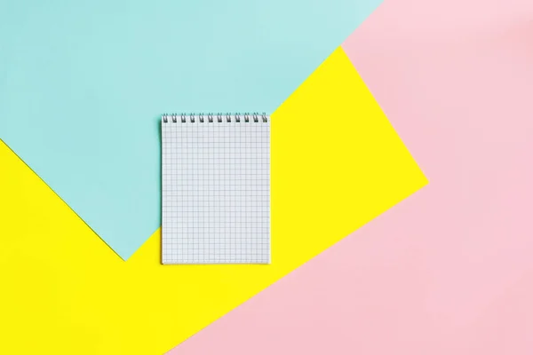 Vista dall'alto di strumenti da ufficio con quaderno bianco su sfondo blu, giallo e rosa. Spazio per testo . — Foto Stock