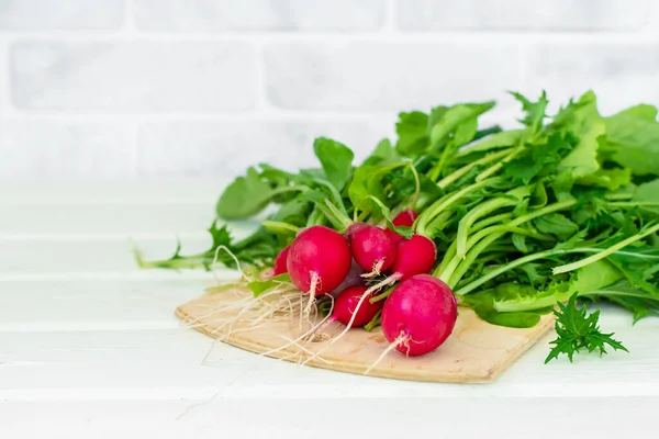 Bunch of round radishes with tops on the white table. White brick wall in the background. Radish is ready for cooking.