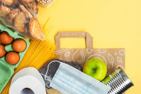 Karantina süresi için yiyecekler, fotokopi alanı olan sarı arka planda yatıyordu. Yumurta, makarna, fasulye, tuvalet kağıdı, elma ve biraz seleal. Kriz gıda malzemeleri. Teslimat, bağış konsepti.