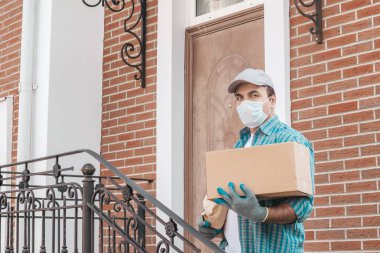 Koruyucu maskeli ve tıbbi eldivenli kurye paket yemek getiriyor. Teslimat servisi karantina altında. Karton kutu ve paket..