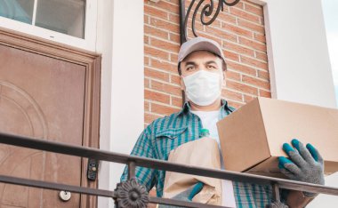 Koruyucu maskeli ve tıbbi eldivenli kurye paket yemek getiriyor. Teslimat servisi karantina altında. Karton kutu ve paket..
