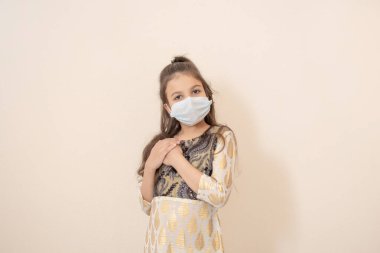 Geleneksel Pakistan kıyafeti ve maskesi giyen ve Ramazan Kareem 'i kutlayan küçük bir kız. Işık taşı arkaplanında izole