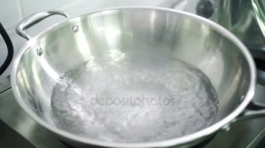 Ocakta kolları su kaynar ile büyük metal bir kase içinde.