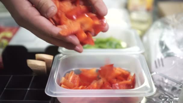 Cuisinière ajoute des poivrons rouges dans des conteneurs pour les blancs sur la table — Video