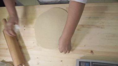 Baker masaüstünde ahşap bir oklava ile hamur rulo.