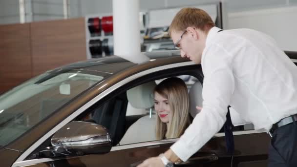 In de showroom vrouw zitten in een bruine auto, die de verkoper zegt. — Stockvideo