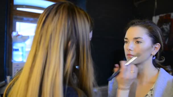 Визажист делает макияж для модели на фотосессии в помещении — стоковое видео