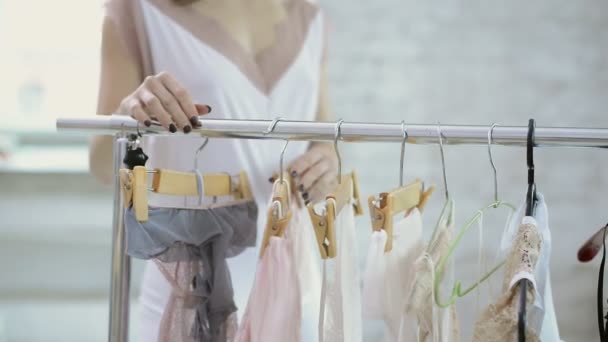 Woman in white clothing comes to rack with hangers to choose clothes — Stock Video