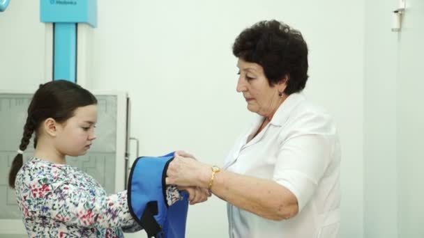 Enfermera ayuda a ponerse chaleco protector en gabinete de rayos X en el hospital — Vídeo de stock