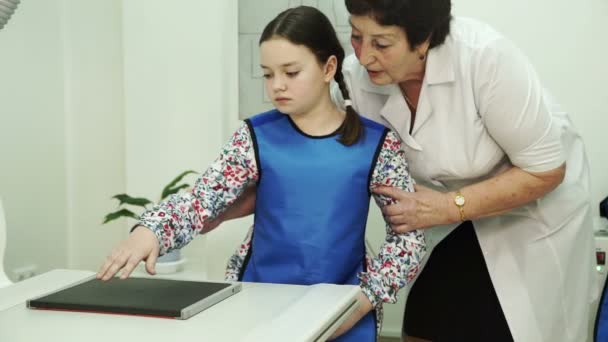 En äldre sjuksköterska förbereder en liten flicka för röntgen penslar. — Stockvideo
