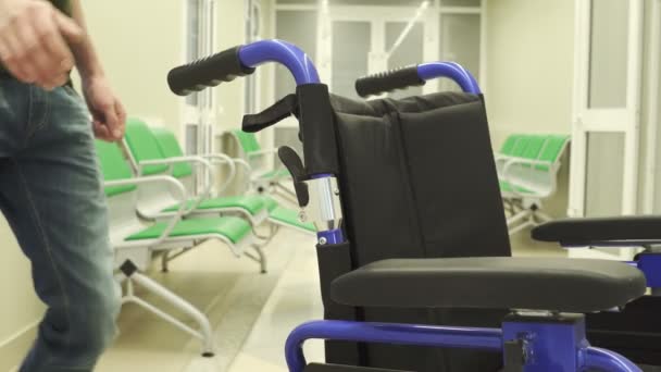 Jonge man beweegt rolstoel in premisse in ziekenhuis. — Stockvideo