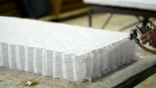 Pracownik kropi klej materiału do produkcji materac w fabryce w pomieszczeniu i odcina nadmiar materiału. — Wideo stockowe