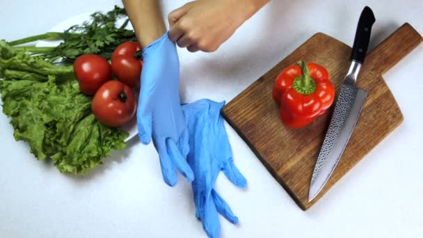Mann zieht Handschuhe am Tisch an, an dem Gemüse in der Küche liegt. — Stockvideo