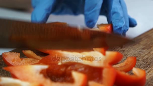 Close-up van de hand in handschoenen is snij met mes in stukken van peper. — Stockvideo