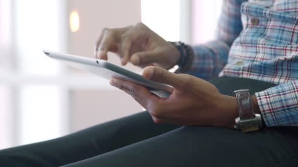 The man fills the form on his tablet while sitting in bright room. — Stock Video