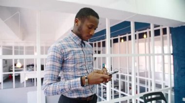 Genç adam smartphone, modern ofiste ayakta kullanıyor.