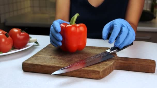 Em tábua de madeira as mãos femininas em luvas de borracha cortam l pimentão doce vermelho . — Vídeo de Stock