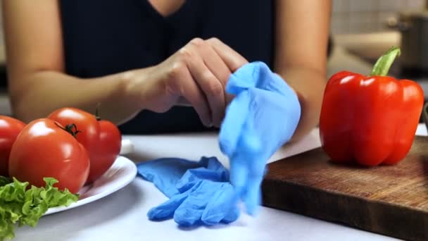 Γυναίκα στο τραπέζι της κουζίνας που βάζει σε αποστειρωμένα γάντια για κοπή λαχανικών. — Αρχείο Βίντεο