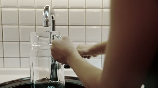 Vrouw vullingen werper met drinkwater uit metalen kraan in keuken van huis. — Stockvideo