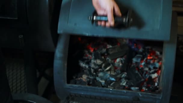 Young man is turning coals in smokehouse oven indoors. — Stock Video