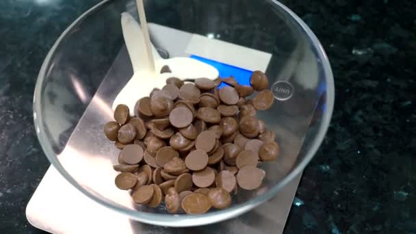 Los trozos de chocolate se están vertiendo con leche grasa en el recipiente de vidrio . — Vídeo de stock