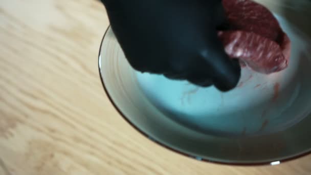 Närbild hand i handskar tar bit rått kött och sätter på bordet. — Stockvideo