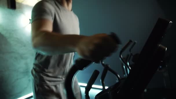 Slim body of young male athlete, who is doing exercise on cross-trainer in modern gym, slow motion. — Stock Video