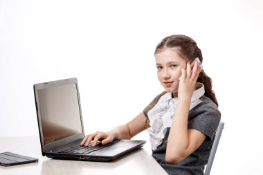 Dizüstü bilgisayarda oturan ve beyaz arka planda telefonla konuşan tatlı bir kız öğrenci.